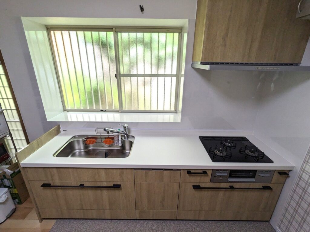 大野城市でキッチンを木目調のLIXILのリシェルにした施工後の画像。天板は白で、取っ手は黒。