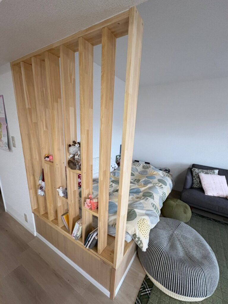 福岡市南区でマンションリフォーム・リノベーションをした施工後の画像。リビングの一画に小上がりを作って下には収納できるようにしました。 布団も敷けるサイズの小上がりなのでお昼寝をしたりもできます。小上がりの一部には、格子を付けて半おこもりスペースにデザインしました。 格子には飾りを置いたりできる工夫もされています。