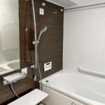 福岡市中央区で浴室リフォームをした施工後の画像。ダークブラウンの木目調のアクセントパネルの高級感と床のラグ調のベージュの床がおしゃれです。